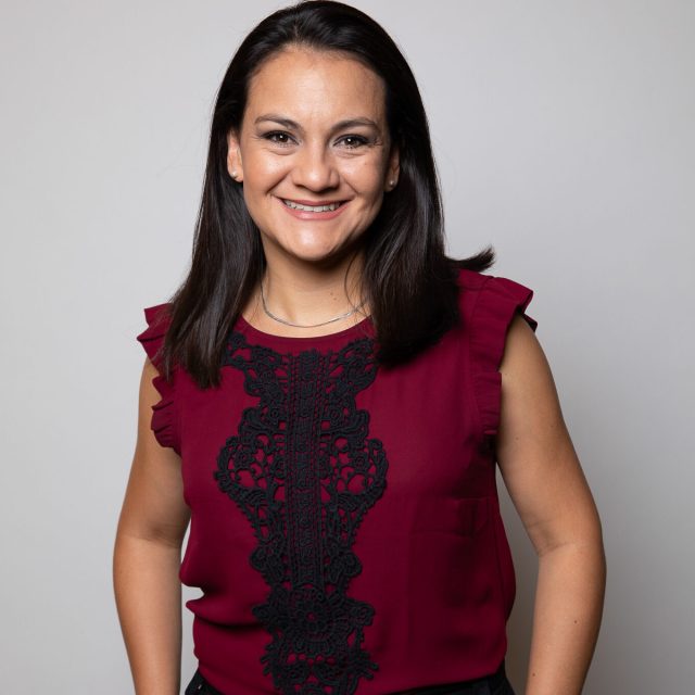 Margarita é uma mulher colombiana de cabelos castanhos escuros lisos na altura dos ombros. Veste uma blusa vermelha e calça preta