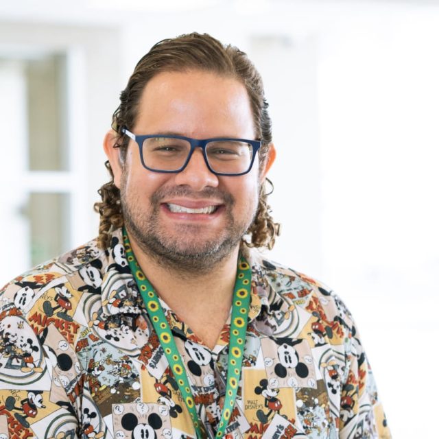 Thierry é um homem branco, de cabelos castanhos encaracolados na altura dos ombros, com óculos e barba